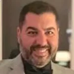 A man with a beard, donning a gray blazer and dark shirt, smiling confidently at the camera, ready to create memorable posts.